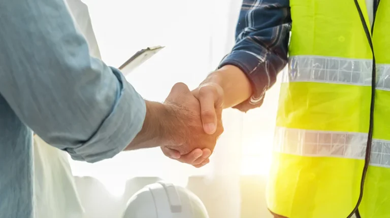 A construction worker in a high vis vest and man in a blue button down shirt shake hands