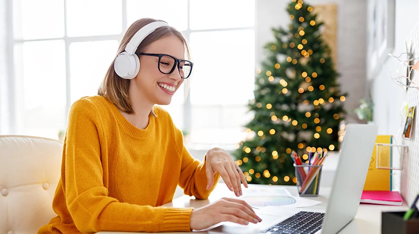 A woman works from home. She's sitting at a desk with a Christmas tree in the background