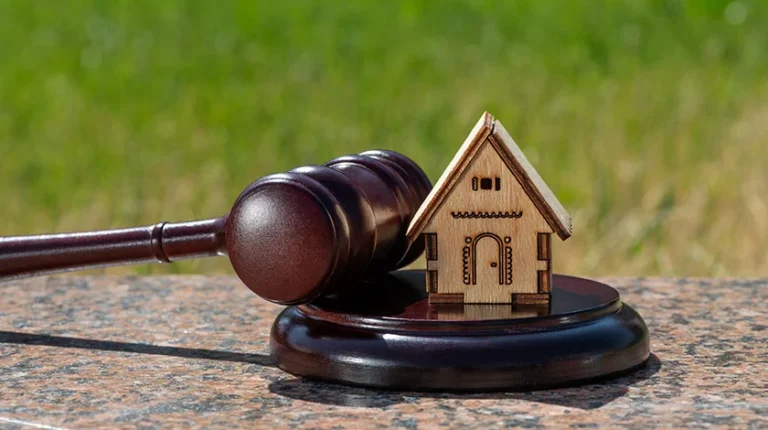 A gavel and a small wooden model of a house are on the ground