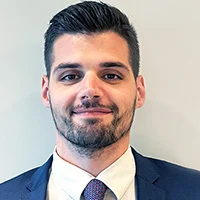 A headshot of Sebastian Flaherty-Tesoriero who works in Family Law. He wears a white shirt, blue tie and blue suit jacket. He has gelled, short black hair and a closely clipped beard and moustaches. He has brown eyes and is smiling.