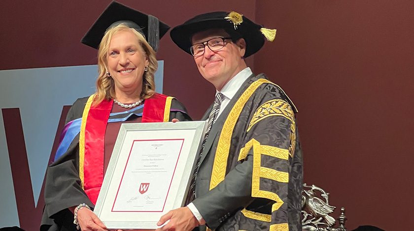 Caroline Hutchinson accepted her Honorary Award from Western Sydney University. She and a man stand on stage in robes holding the framed certificate.