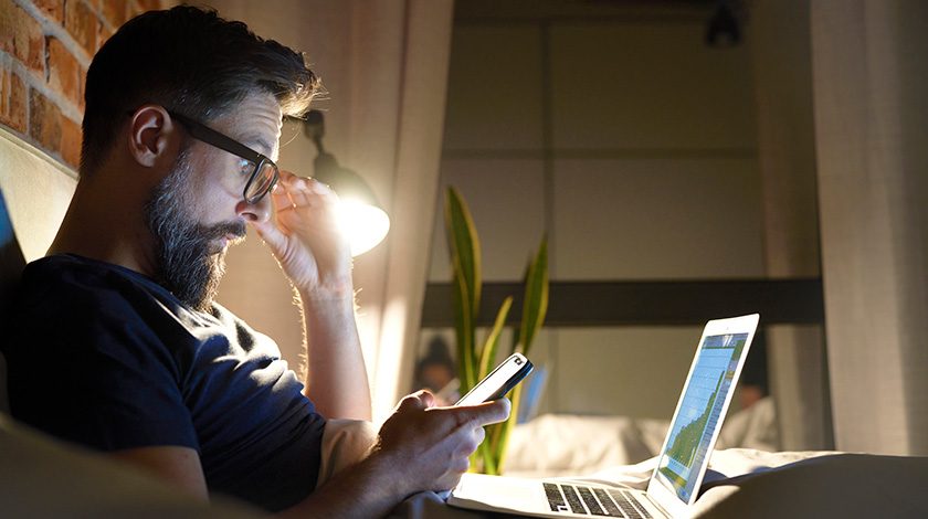 A man with glasses stares at a brightly lit laptop screen