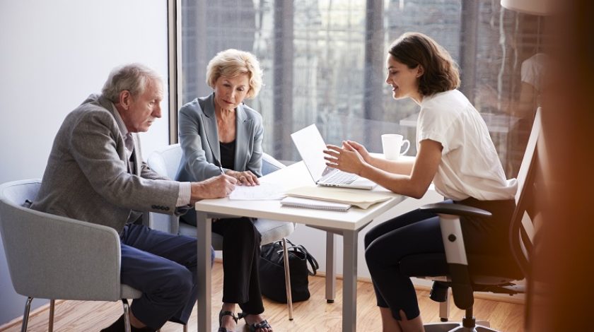 Senior Couple Signing Document In Meeting With Female Financial Advisor In Office