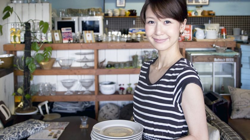 A young waitress carries some of white small dishes in a restaurant. She is preparing for the business hours of the shop.