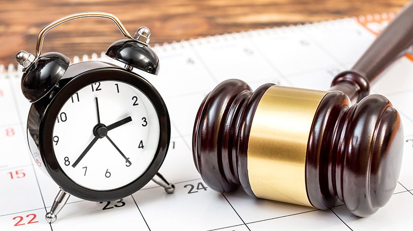 An alarm clock and gavel sit upon a calendar on a desk