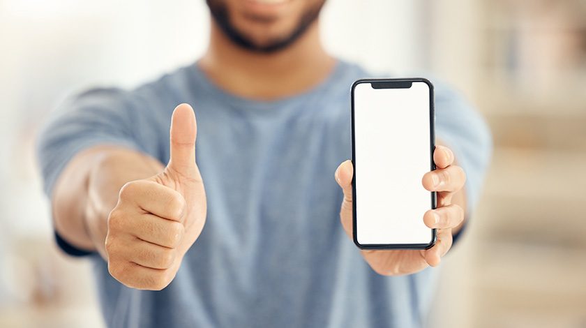 A man in a blue shirt holds a phone in one hand and has a thumbs up with the other.