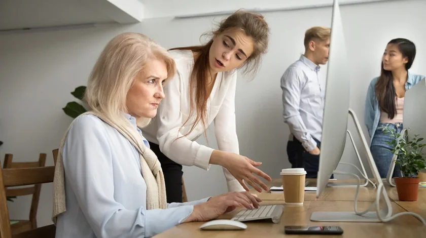 Young team leader correcting offended senior employee working on computer in office, female manager scolding aged old worker for mistake or incompetence, different generations and age discrimination