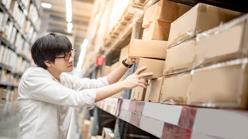 Young Asian man picking paper box from shelf in warehouse, shopping warehousing or packing products concepts