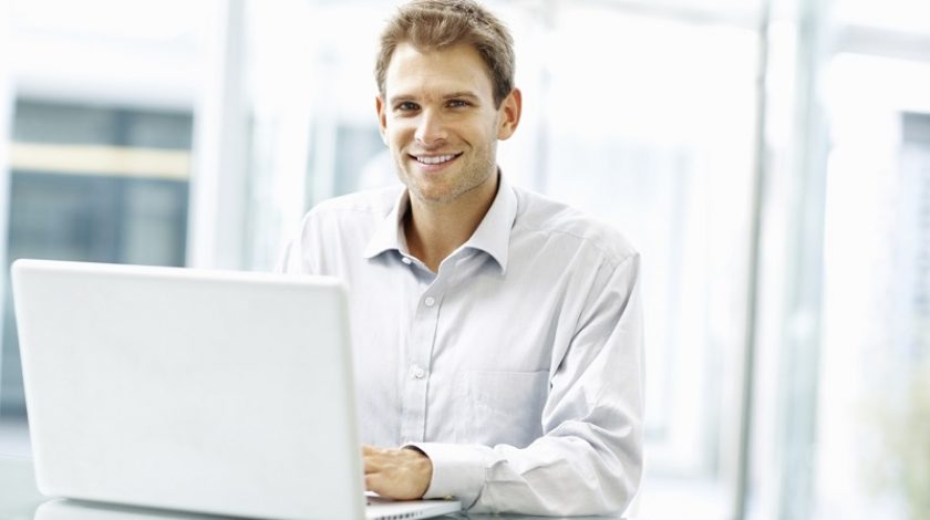 Young good looking executive smiling and working on laptop