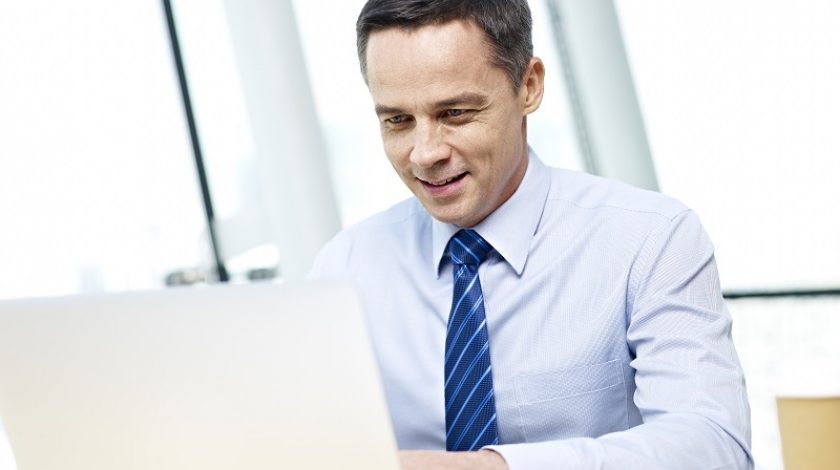 caucasian businessman in shirt and tie working on laptop computer in office and smiling.